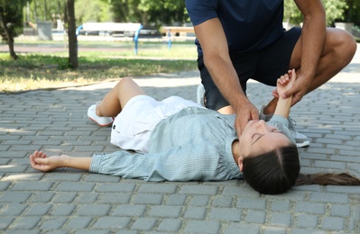Man checking pulse of unconscious young woman outdoors. First aid