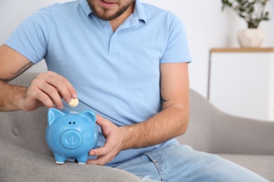 Young man putting coin into piggy bank in living room