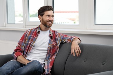 Smiling bearded man looking away on sofa indoors