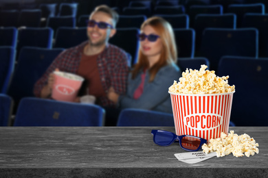Popcorn, 3D glasses, tickets on table and young couple in cinema hall, space for text 