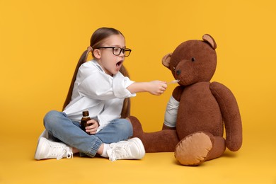 Photo of Little girl playing doctor with toy bear on yellow background