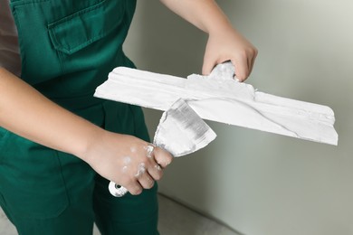 Professional worker holding putty knives with plaster indoors, closeup