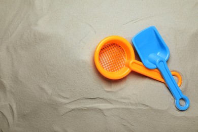 Plastic toy shovel and sieve on sand, flat lay