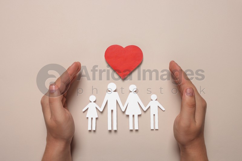 Photo of Man protecting paper family figures and red heart on beige background, top view. Insurance concept