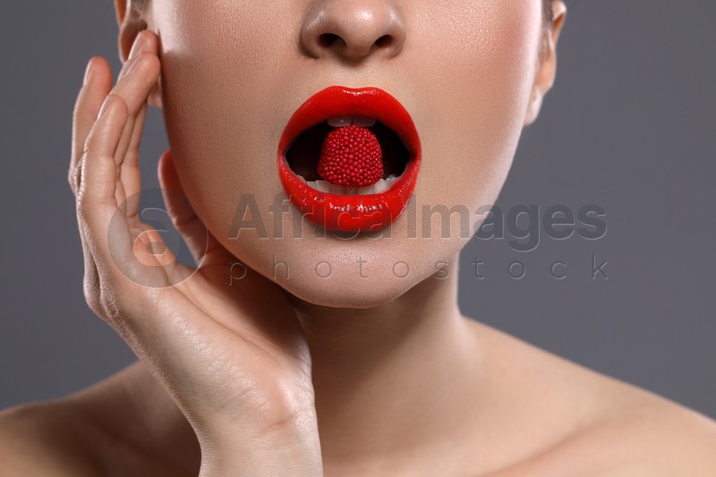 Young woman with red lips makeup eating candy on grey background, closeup
