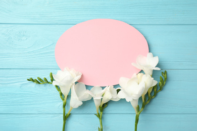 Beautiful spring freesia flowers and blank card on blue wooden table, flat lay. Space for text