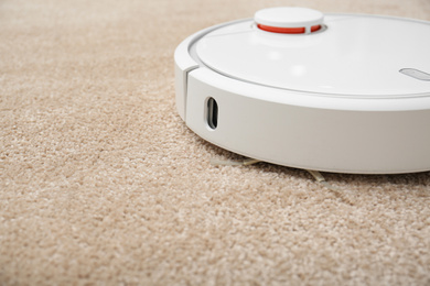 Removing dirt from carpet with modern robotic vacuum cleaner indoors, closeup