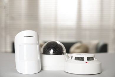 Photo of CCTV camera, smoke and movement detectors on white table indoors. Home security system