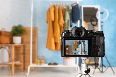 Photo of Rack with stylish clothes and mirror near light blue wall indoors, focus on camera screen. Space for text