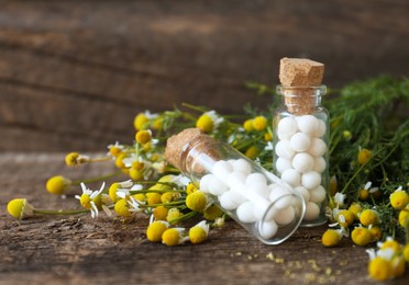 Bottles with homeopathic remedy and chamomile flowers on wooden table, closeup. Space for text