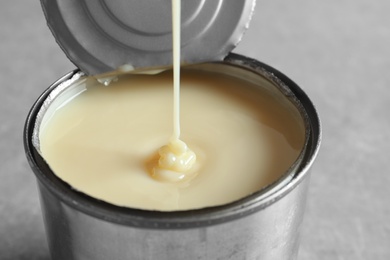 Condensed milk pouring into tin can on   grey background, closeup. Dairy product