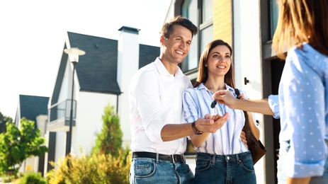 Real estate agent giving house keys to young couple outdoors