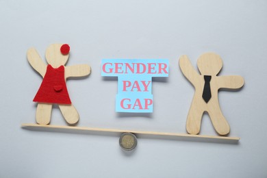 Photo of Gender pay gap. Wooden figures of man and woman on miniature seesaw against light grey background
