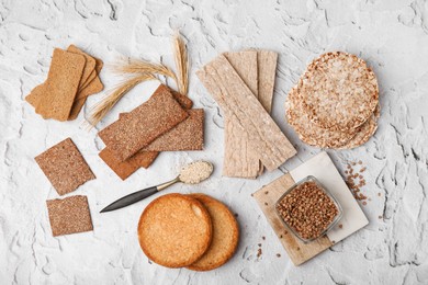 Rye crispbreads, rice cakes and rusks on white textured table, flat lay