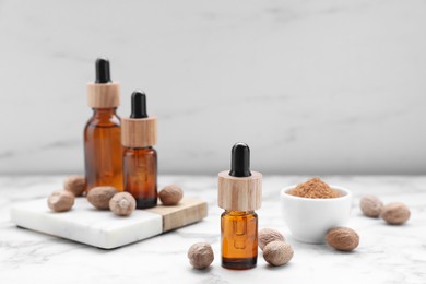 Photo of Bottles of nutmeg oil and nuts on white marble table