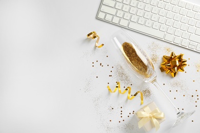 Composition of champagne glass with gold glitter, keyboard and gift box on white background, top view. Hilarious celebration