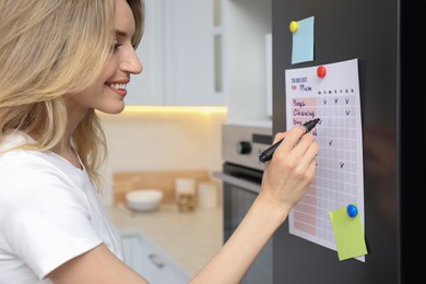 Young woman checking to do list on refrigerator door in kitchen