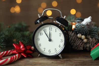 Vintage alarm clock and decor on wooden table against blurred Christmas lights, closeup. New Year countdown
