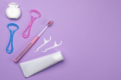 Flat lay composition with tongue cleaners and teeth care products on violet background, space for text
