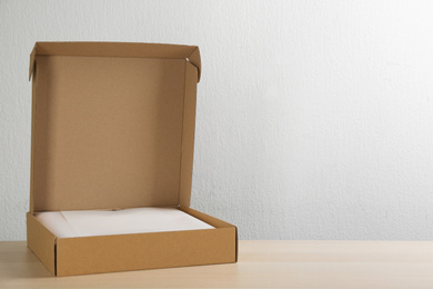 Open cardboard box on wooden table against light background. Space for text