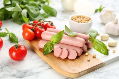 Fresh raw vegetarian sausages with basil, soybeans and vegetables on white marble table