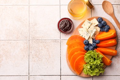 Photo of Delicious persimmon, blue cheese and blueberries on tiled surface, flat lay. Space for text