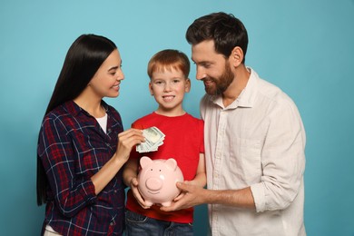 Happy family putting money into piggy bank on light blue background