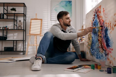Young man painting on canvas with brush in artist studio