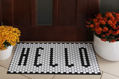 Stylish door mat with word HELLO and beautiful flowers on floor