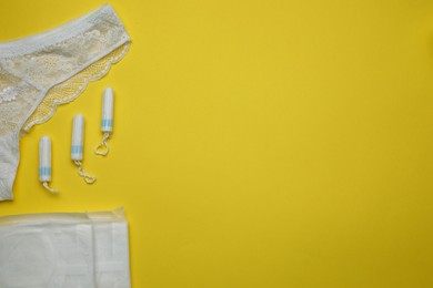 Woman's panties, menstrual pads and tampons on yellow background, flat lay. Space for text