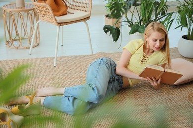 Happy young woman reading book on floor at indoor terrace