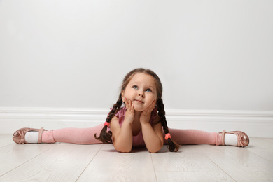 Photo of Cute little girl on floor near light grey wall