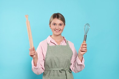 Photo of Beautiful young woman in clean apron with kitchen tools on light blue background