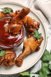 Photo of Delicious fried chicken wings served with parsley and sauce on table, above view