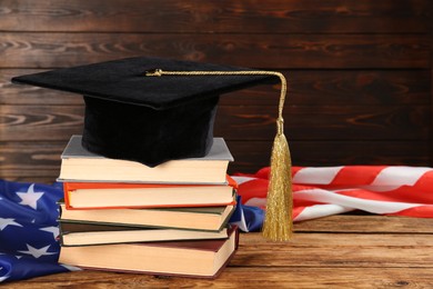 Graduation hat, books and American flag on wooden table. Space for text