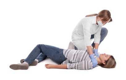 Doctor in uniform and protective mask performing first aid on unconscious woman against white background