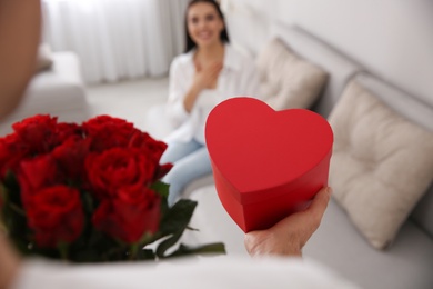 Man presenting gift and bouquet to his beloved woman at home, closeup. Valentine's day celebration