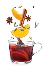 Cut orange and different spices falling into glass cup of mulled wine on white background 
