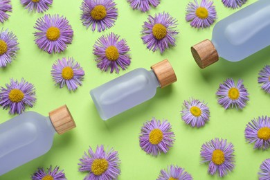 Flat lay composition with bottles of essential oil and daisy flowers on light green background