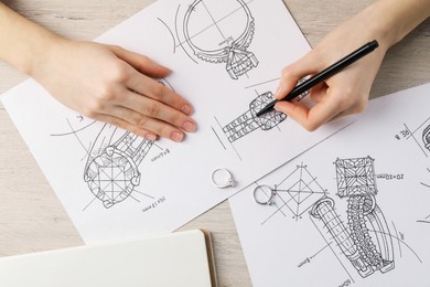 Photo of Jeweler drawing sketch of elegant ring on paper at wooden table, top view