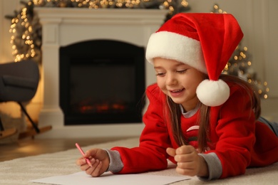 Cute child writing letter to Santa Claus while lying on floor at home, space for text. Christmas celebration