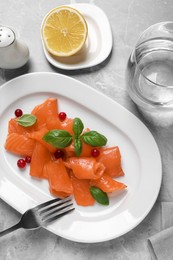 Photo of Salmon carpaccio with cranberries and basil served on grey table, flat lay
