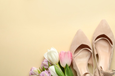 Stylish shoes and beautiful flowers on beige background, flat lay. Space for text