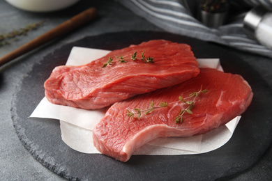 Fresh raw beef cut with thyme on grey table, closeup