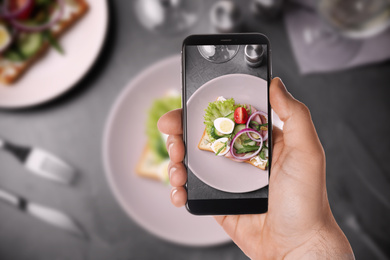 Blogger taking picture of delicious sandwich with ham at table, closeup. Food photography