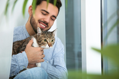 Man with tabby cat near window at home. Friendly pet