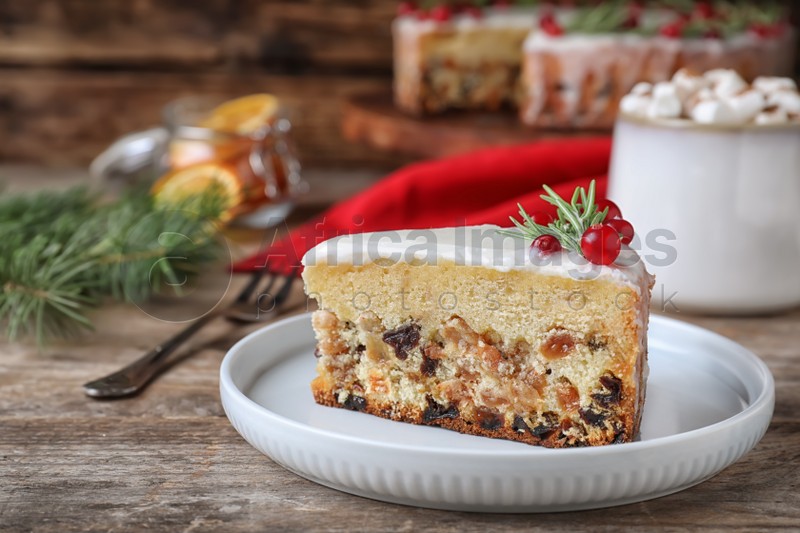 Slice of traditional Christmas cake decorated with rosemary and cranberries on wooden table