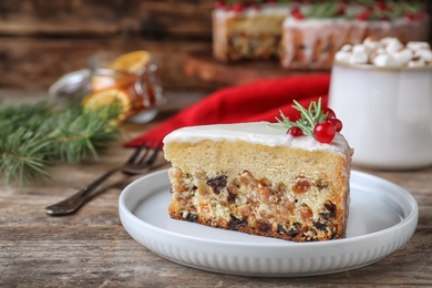 Slice of traditional Christmas cake decorated with rosemary and cranberries on wooden table