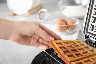 Woman taking Belgian waffles from iron on table, closeup