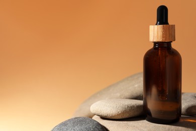 Photo of Bottle of face serum and spa stones on beige background, closeup. Space for text
